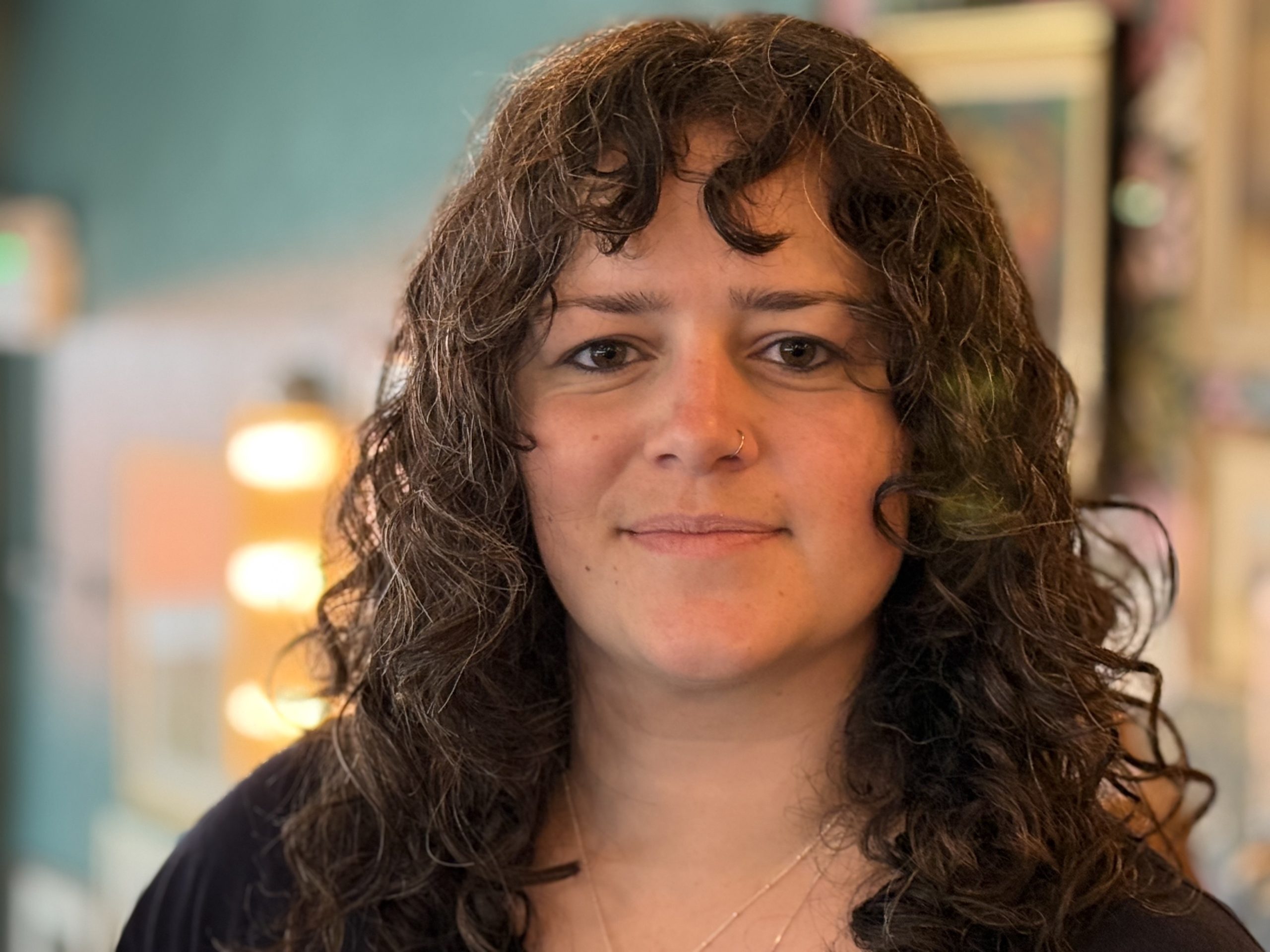 Fi, the therapist and counsellor, looks directly into the camera with an open face and a smile. She has curly brown hair and brown eyes. She is showing that she is friendly and warm and encouraging clients to try counselling and psychotherapy with her.
